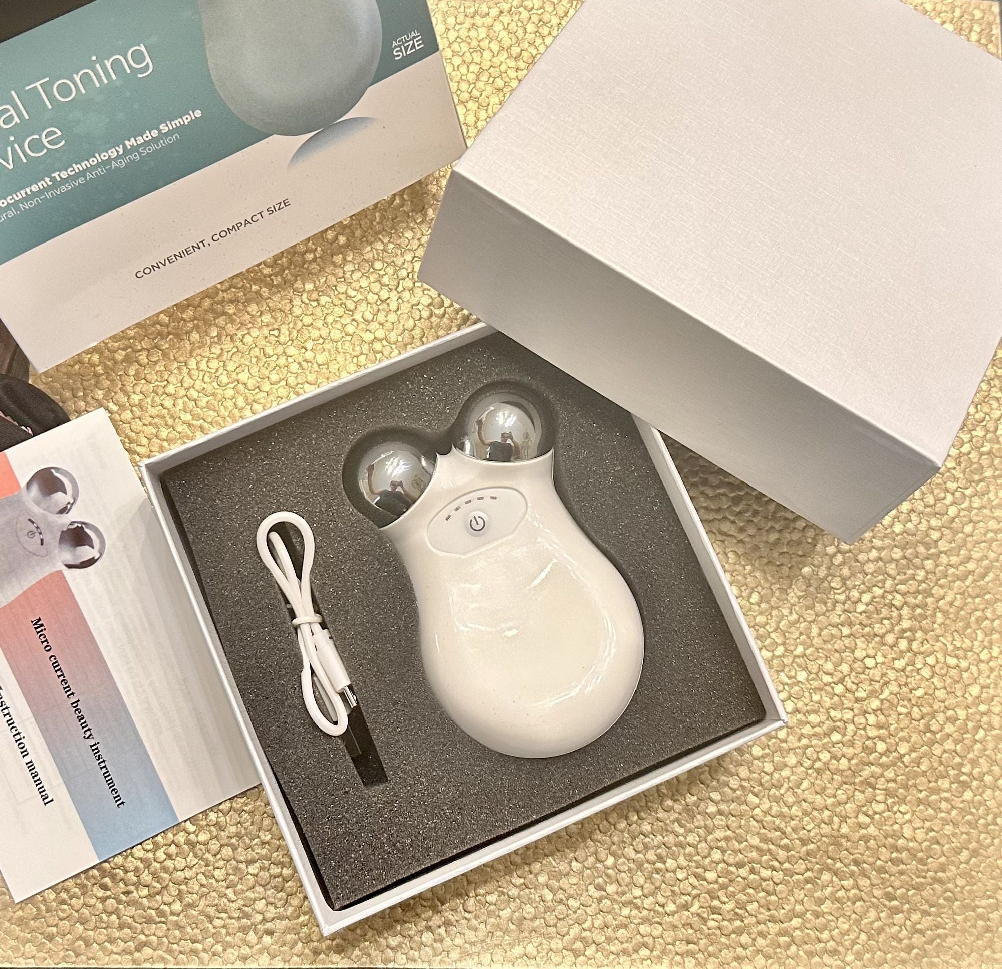 White microcurrent facial massager with USB cable and packaging